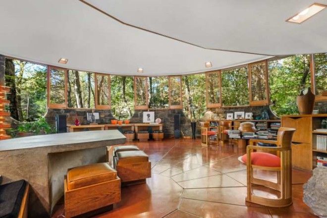 The Sol Friedman House living room is filled with wooden chairs, a stone table, and short shelves.