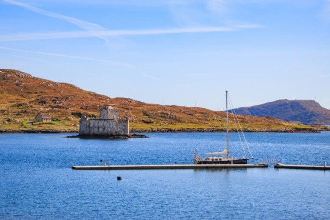 Kisimul Castle on the island of Barra one of the outer hebrides islands and a sailing boat moored on the new marina poonton