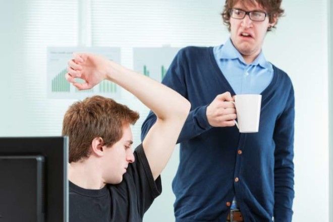 Man smelling his armpits in front of a coworker